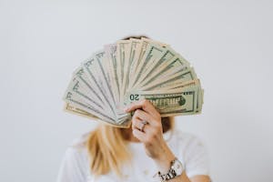 Close-up of a person holding a fan of US dollar bills on a neutral background.