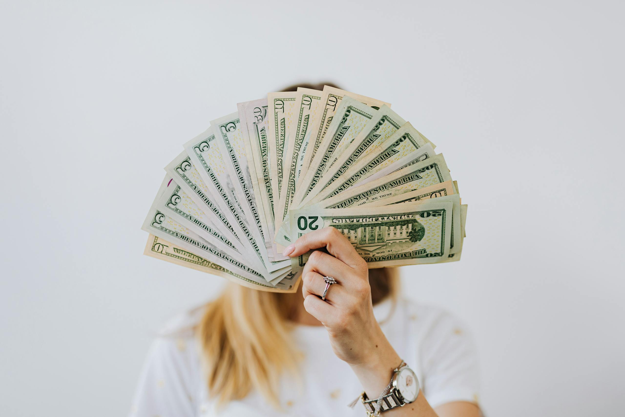 Close-up of a person holding a fan of US dollar bills on a neutral background.