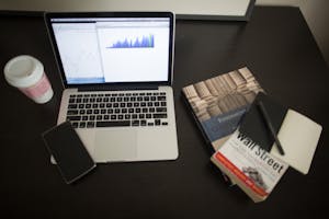 Top view of a desk with laptop, charts, books, and coffee, depicting a modern financial workspace setup.